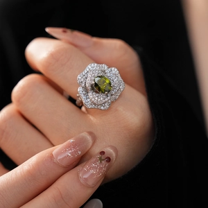 Macro detail of silver flower ring featuring an oval olive green gem and pavé diamonds