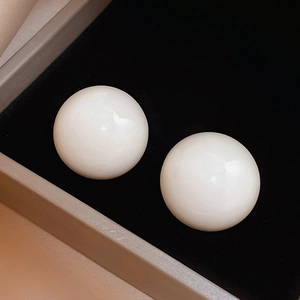 Detailed close-up of glossy white spherical stud earrings on premium black velvet