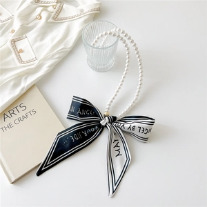 Detail of pearl necklace with black and white striped ribbon bow on white tabletop