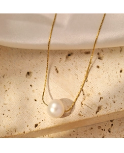 Elegant gold necklace with a single white pearl displayed on stone and silk background