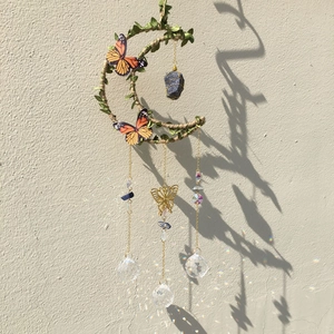 Moon shaped wind chime with green leaves and blue crystal casting light on a white wall