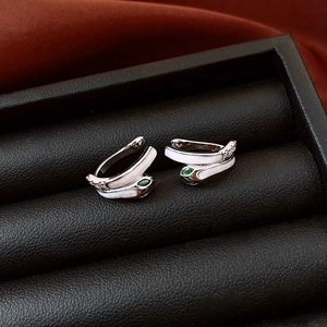 Macro detail of silver snake ear cuff with white inlay and green gemstone eyes