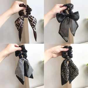 Detail view of four patterned hair scrunchies with long ribbons in diverse textures