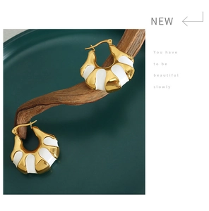 Artistic close-up of C-shaped 18K gold plated hoop earrings with white enamel on wood