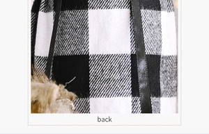 Detail showing buffalo plaid fabric texture, black strap and plush pompom on the bag back