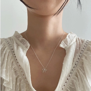 Elegant 925 sterling silver bow pendant necklace worn by a model on a white lace dress