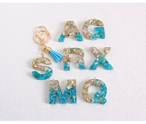 Close-up of glitter resin letter keychains with turquoise stones and blue tassels