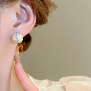 Close-up of a matte white sphere stud earring with a brushed finish on a model's ear