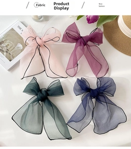 Close-up of four organza bow hair clips in pink, purple, green, and navy on a white tray