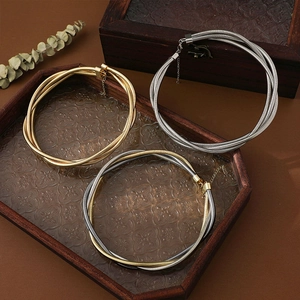 Three-strand coiled metal choker necklaces in gold and silver finish on a wooden tray