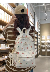 White school backpack with strawberry print and plush ball shown in a retail store scene