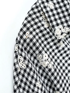 Gros plan détaillé d'une broderie de marguerite blanche sur une chemise à carreaux vichy