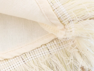 Close-up of cream textile edge featuring dense tassels and gold thread decorative details