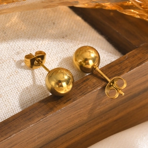 Macro shot of polished gold ball stud earrings on white fabric and dark wood