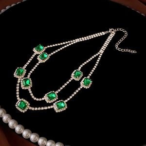Detailed close-up of emerald green square gems and crystal rhinestones on a double necklace