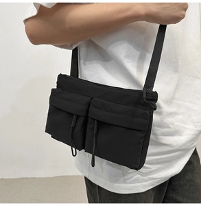 Detail of black nylon messenger bag with dual utility pockets and drawstring zippers