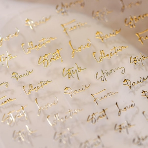 Macro shot of 3D embossed gold butterfly nail stickers with cursive Paris style text