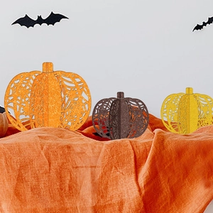 Three glittery cutout paper pumpkins in orange and gold for Halloween party table decor