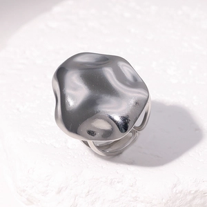 Bague ouverte argentée en acier inoxydable avec texture fluide posée sur socle en pierre