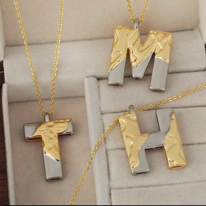 Three two-tone gold and silver alphabet necklaces in a premium jewelry display box