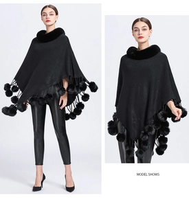 Detailed model view of a black knitted poncho with faux fur collar and tassel pom-poms