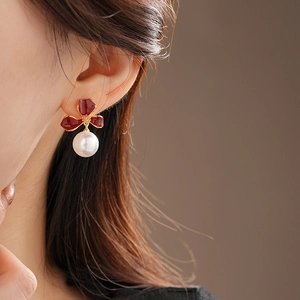 Macro detail of a dark red floral earring with a white pearl drop on a female model