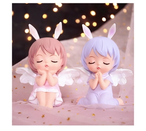 Close-up of pink and purple praying angel figurines with rabbit ears and wings on starry tulle