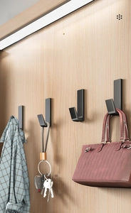 Dark grey matte wall hooks holding a shirt, keys, and a bag on a wood panel background