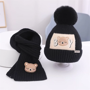 Detail der schwarzen Kinder-Strickmütze und Schal-Set mit Bären-Aufnäher und Bommel