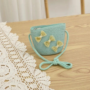 Detail of mint green woven crossbody bag with yellow lace bows on a wooden surface