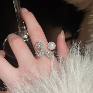Detailed close-up of zircon bow pearl ring on finger with luxury aesthetic accessories