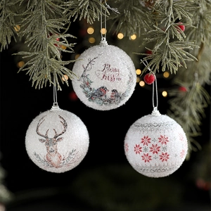 Three white Christmas ornaments with glitter, deer print, and Merry Kissmas hanging on a tree