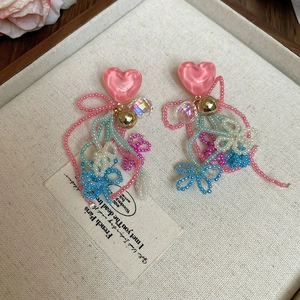 Detail of pink heart resin earrings with colorful seed bead tassels on a soft tray