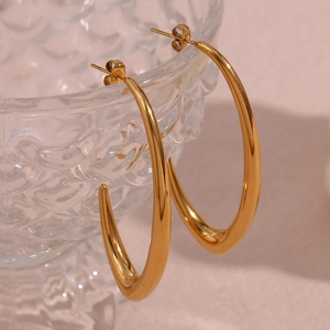 Detailed close-up of large polished gold V-shaped drop earrings on a glass rim