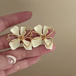 Close-up of double-layer hollow flower earrings with white enamel and gold plating