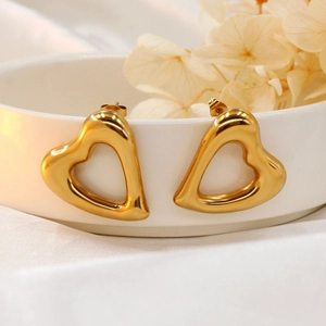 Close-up of gold-plated heart earrings placed on a white ceramic plate with dried flowers