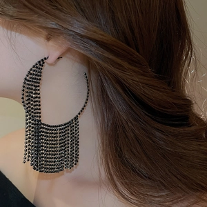 Detailed view of oversized black rhinestone tassel hoop earrings worn by a model