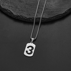 Macro detail of silver stainless steel pendant with hollow number 3 on dark stone background