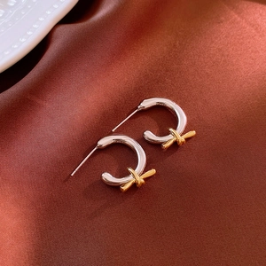 Close-up of C-shaped silver earrings with golden knot detail on dark satin fabric