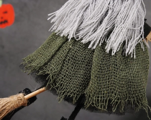 Detail of witch doll with grey hair, green burlap dress, and small wooden broom accessory