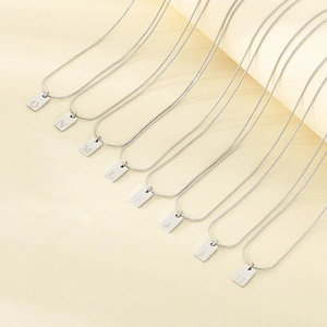 Macro-opname van zilveren vierkante letterhangers O-H aan elegante slangenkettingen