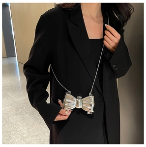 Silver metallic bow-shaped crossbody bag with a slim chain strap worn on a black blazer