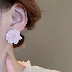 Pink acrylic cherry blossom earrings with pearl core shown worn on model's ear