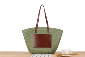 Close-up of green woven straw tote bag with brown leather pocket on a wooden surface