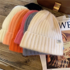 Detailed pile of colorful ribbed knit beanies in white, pink, and blue on wood