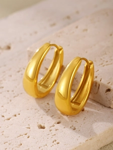 Close-up of polished gold oval hoop earrings on a textured stone pedestal