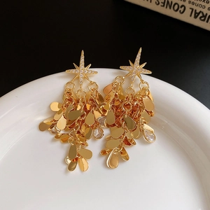 Détail de boucles d'oreilles pompons dorées avec motifs d'étoiles et oxydes de zirconium