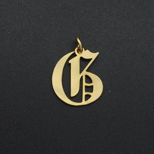 Detailed view of a gold gothic letter G pendant with a hanging ring on black surface