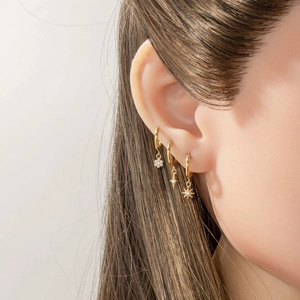 Titanium hoop earrings with gold floral star and sun charms on a model's ear