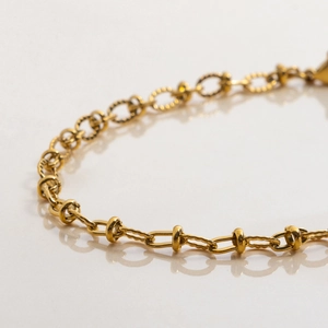 Macro detail of gold-plated chain bracelet featuring spiral texture and rectangular links